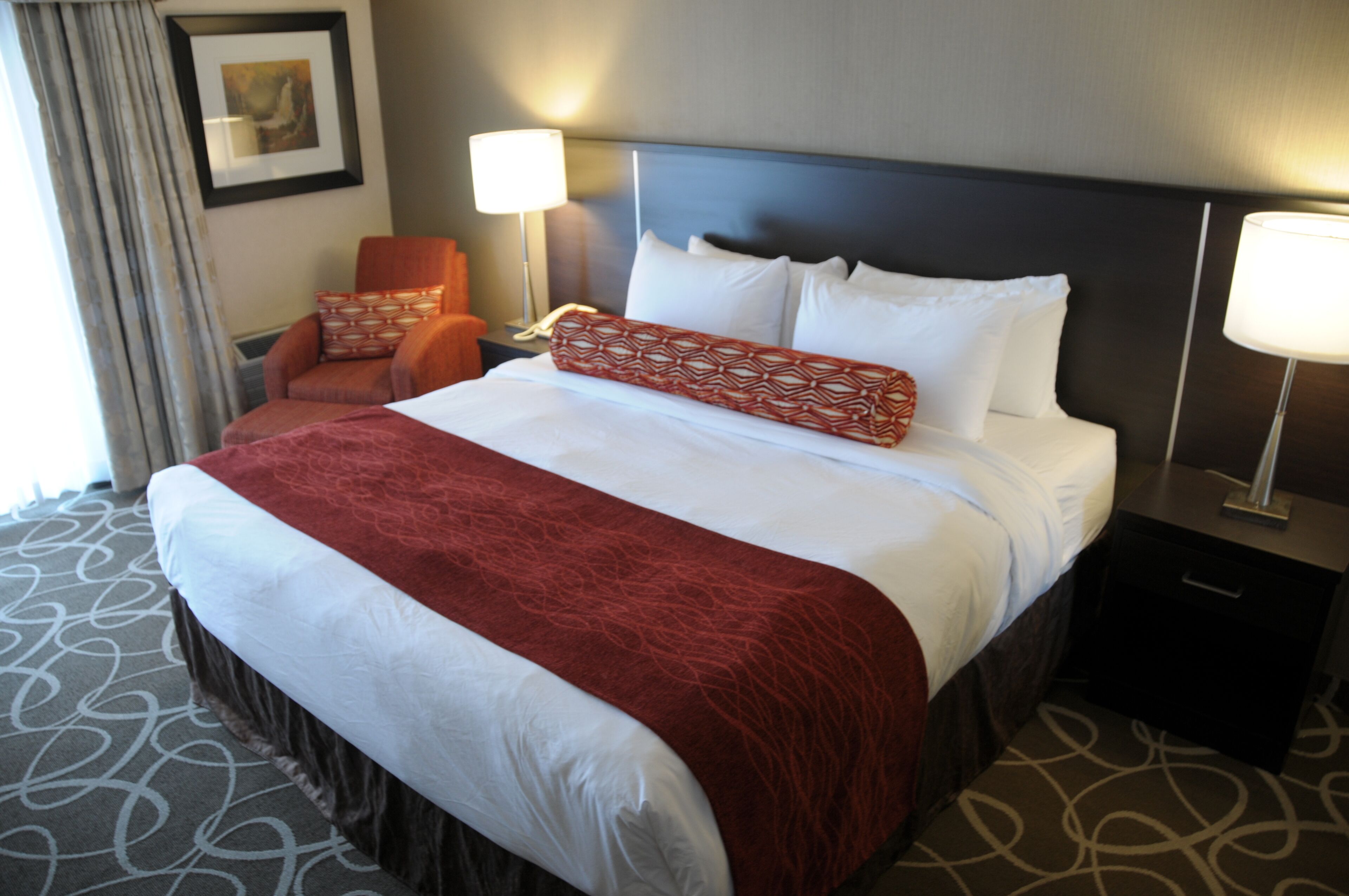 A hotel room with a large bed, two bedside lamps, a chair, and a nightstand.