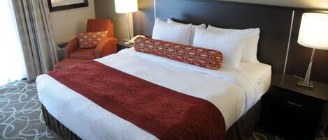 A hotel room with a large bed, two bedside lamps, a chair, and a nightstand.