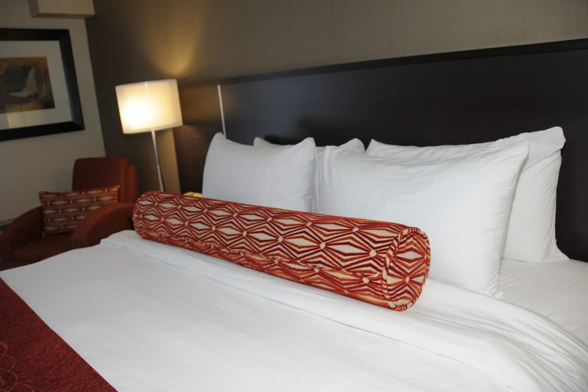 A neatly made bed with white linens and a red patterned pillow.