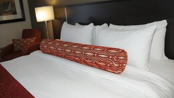 A neatly made bed with white linens and a red patterned pillow.
