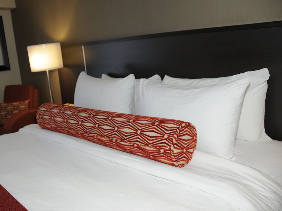 A neatly made bed with white linens and a red patterned pillow.