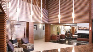 A spacious lobby with a high ceiling, wooden slats, and a central seating area with a coffee table and chairs.