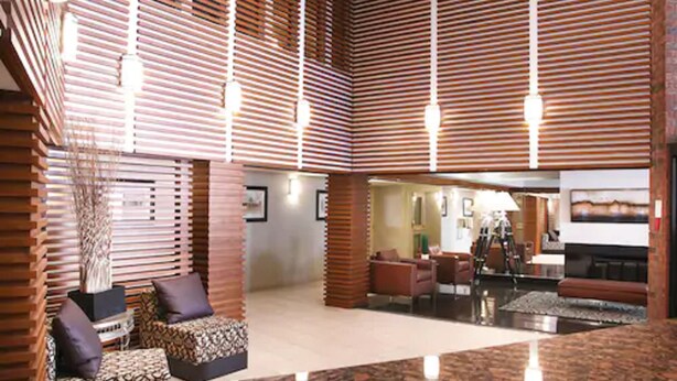 A spacious lobby with a high ceiling, wooden slats, and a central seating area with a coffee table and chairs.