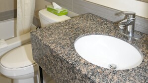 A bathroom with a white toilet, a sink with a granite countertop, and a shower with a white curtain.