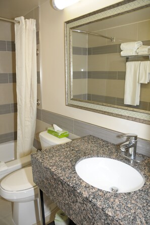 Un baño con inodoro blanco, lavabo con encimera de granito y ducha con cortina blanca.