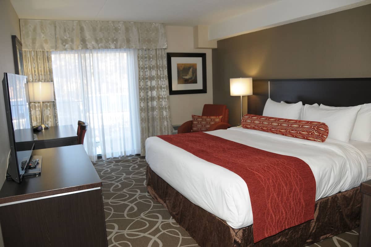A hotel room with a large bed, a desk with a TV, a chair, a lamp, and a framed picture on the wall.