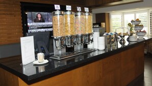 A self-serve coffee station with multiple dispensers, a television screen, and a menu sign.