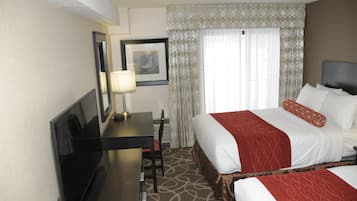 Una habitación de hotel con cama, escritorio, silla, televisor y ventana con cortinas.