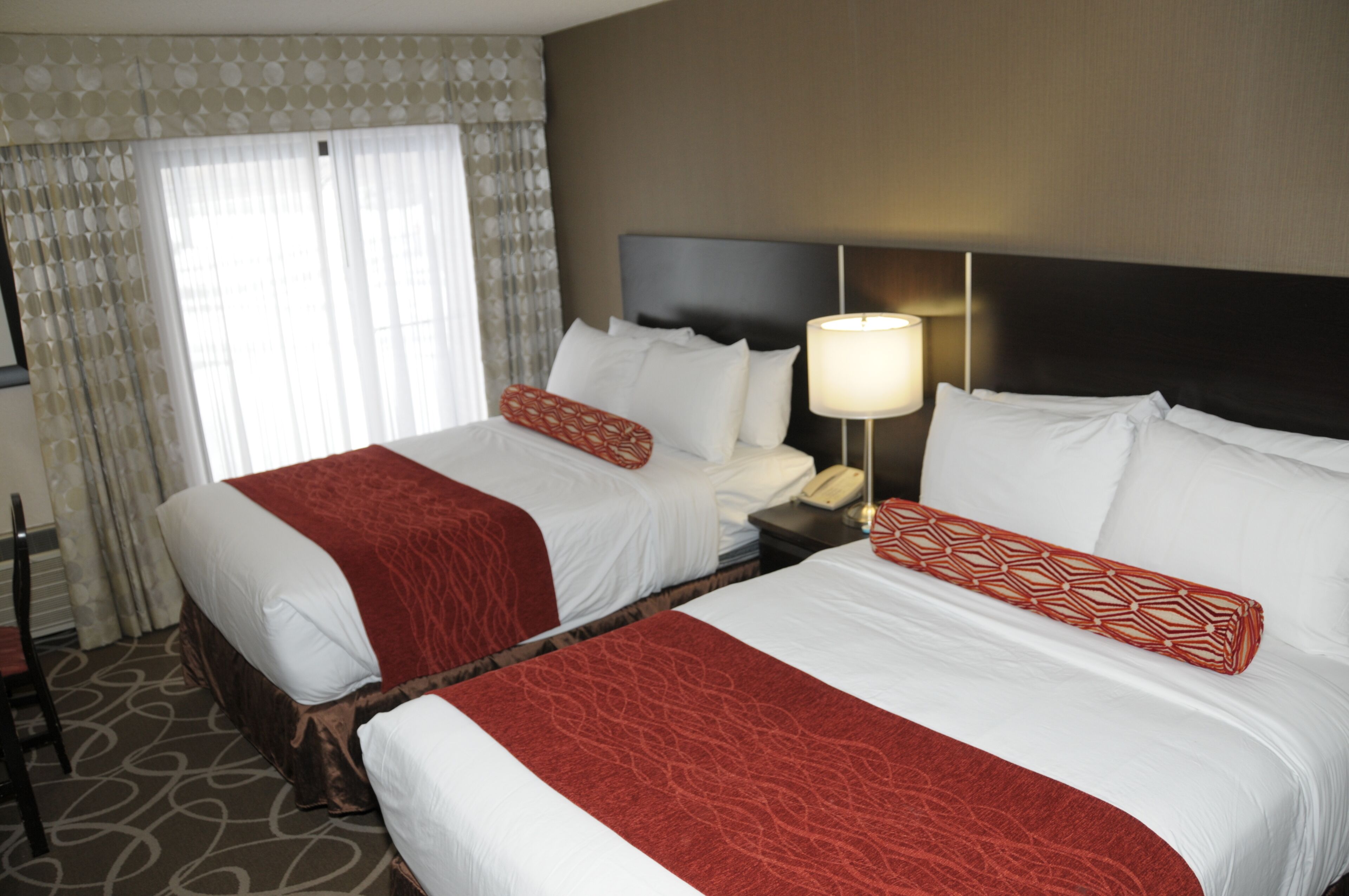 A hotel room with two beds, a nightstand with a lamp, and a telephone.