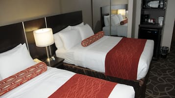 Een hotelkamer met twee bedden, elk voorzien van witte lakens en rode sierkussens. Er staat een nachtkastje met een lamp en een klein tafeltje met een koffiezetapparaat en kopjes. Boven de bedden hangt een spiegel aan de muur.