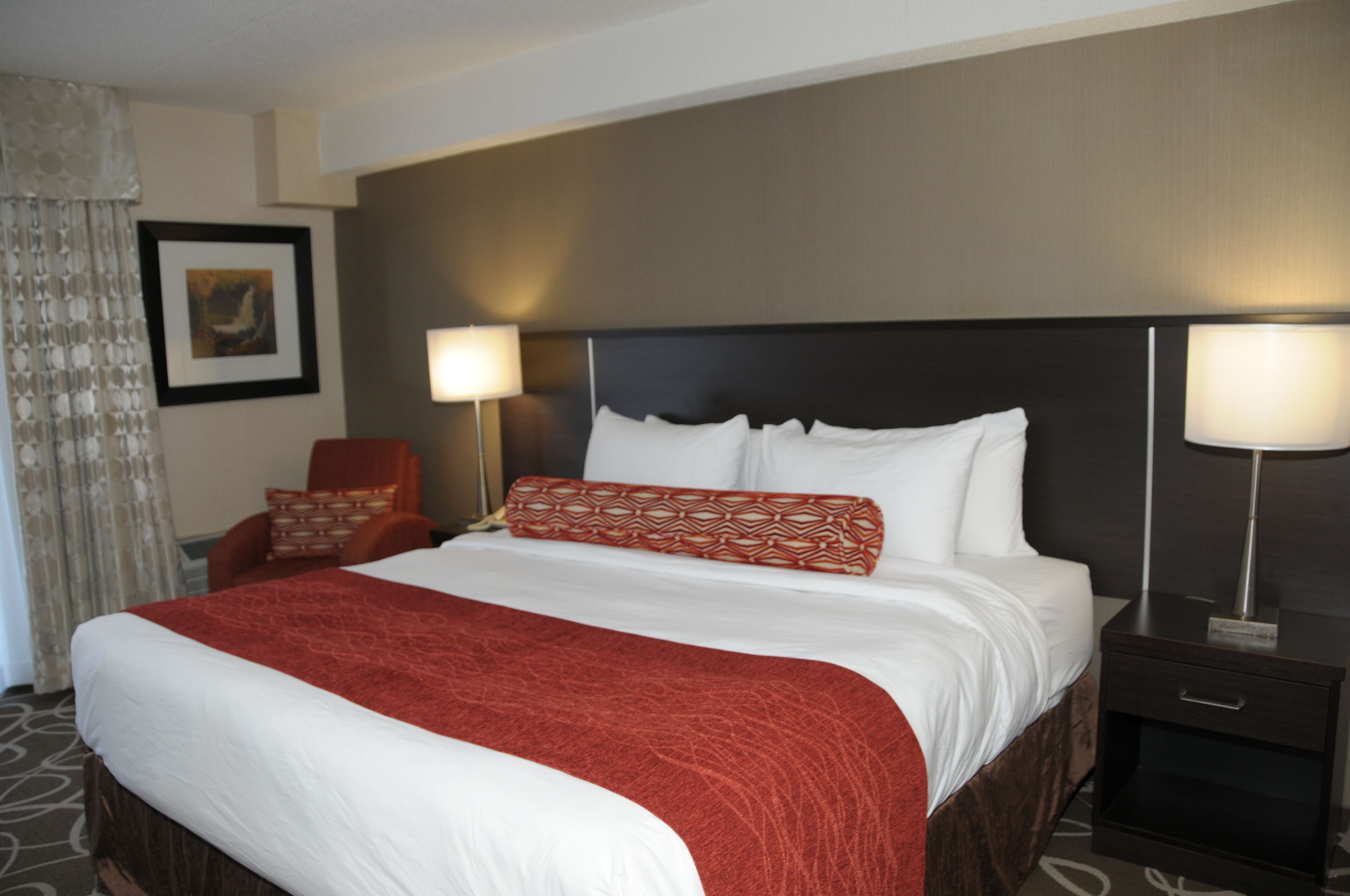 A hotel room with a large bed, two bedside lamps, a chair, and a framed picture on the wall.