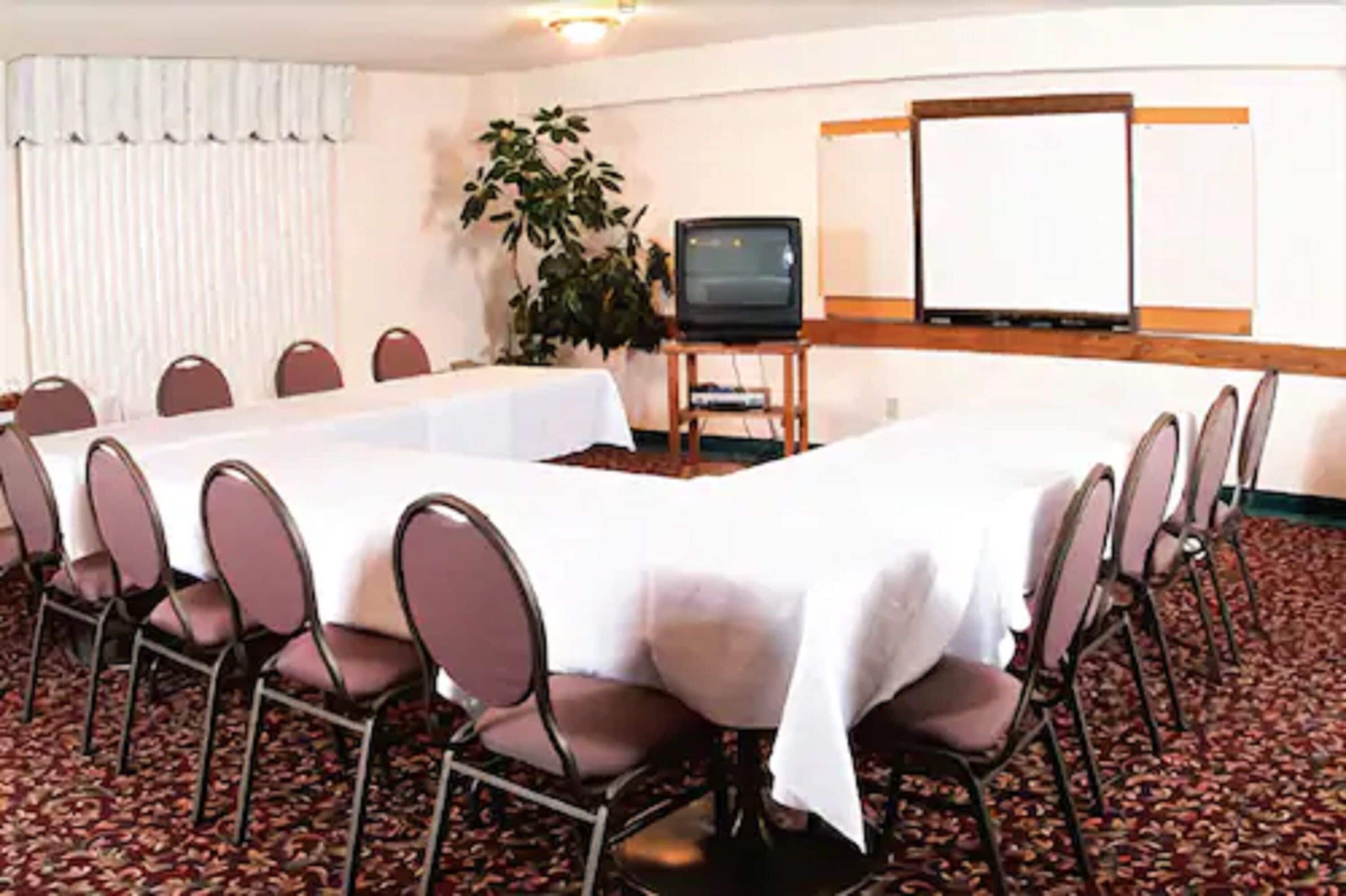 Un salón de conferencias con una larga mesa, sillas, una pantalla de proyector y un televisor.