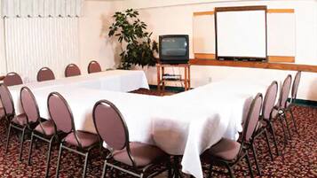 Un salón de conferencias con una larga mesa, sillas, una pantalla de proyector y un televisor.