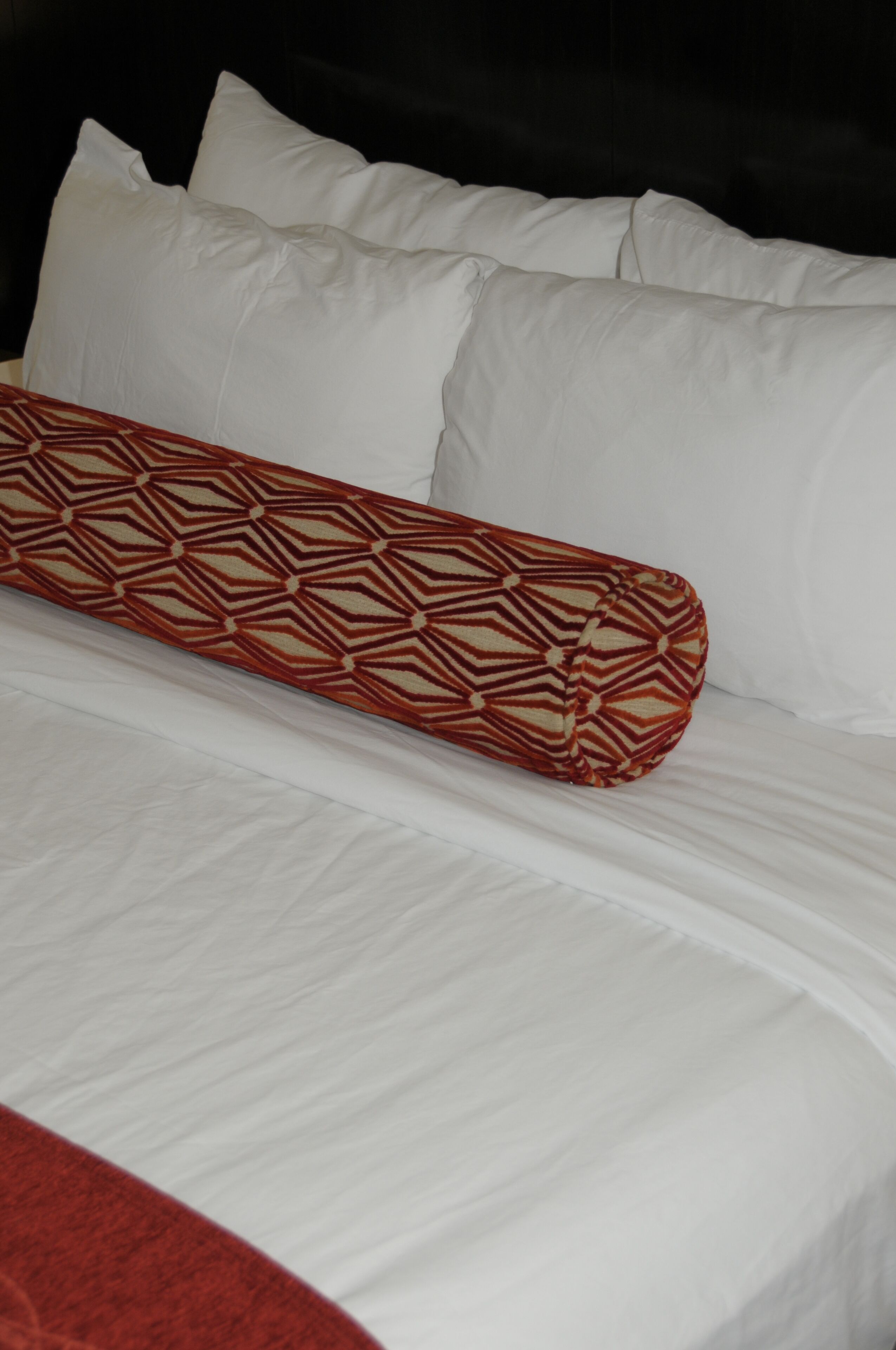 Una cama con sábanas blancas y una almohada estampada.