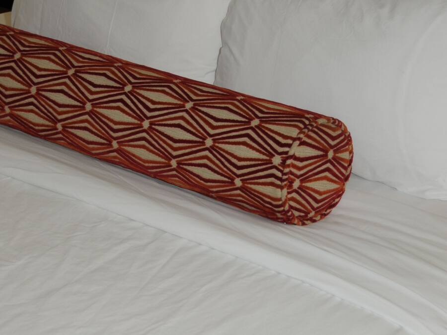 Una cama con sábanas blancas y una almohada estampada.