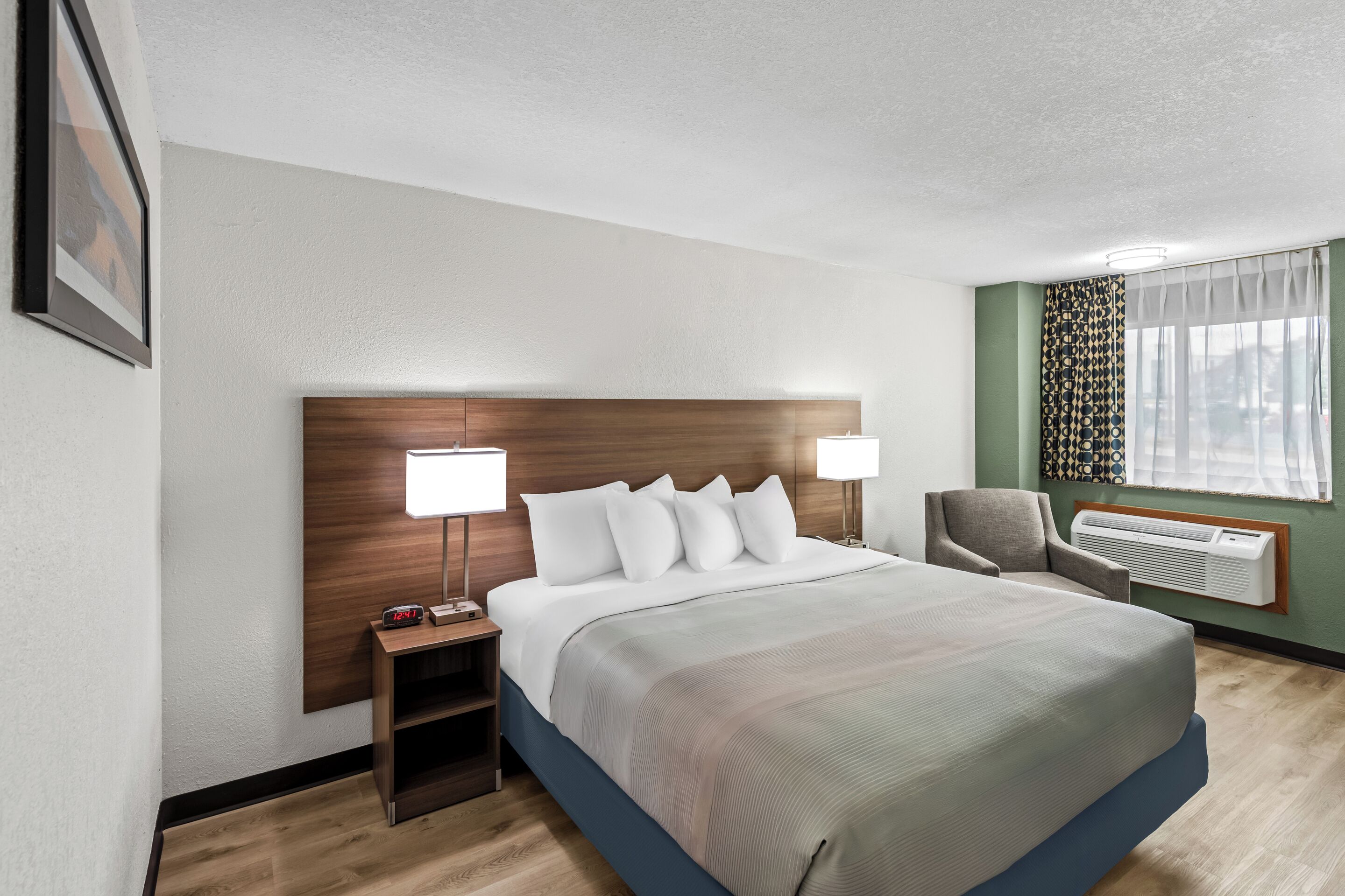 A hotel room with a large bed, bedside lamps, a chair, a desk, and a window with curtains.