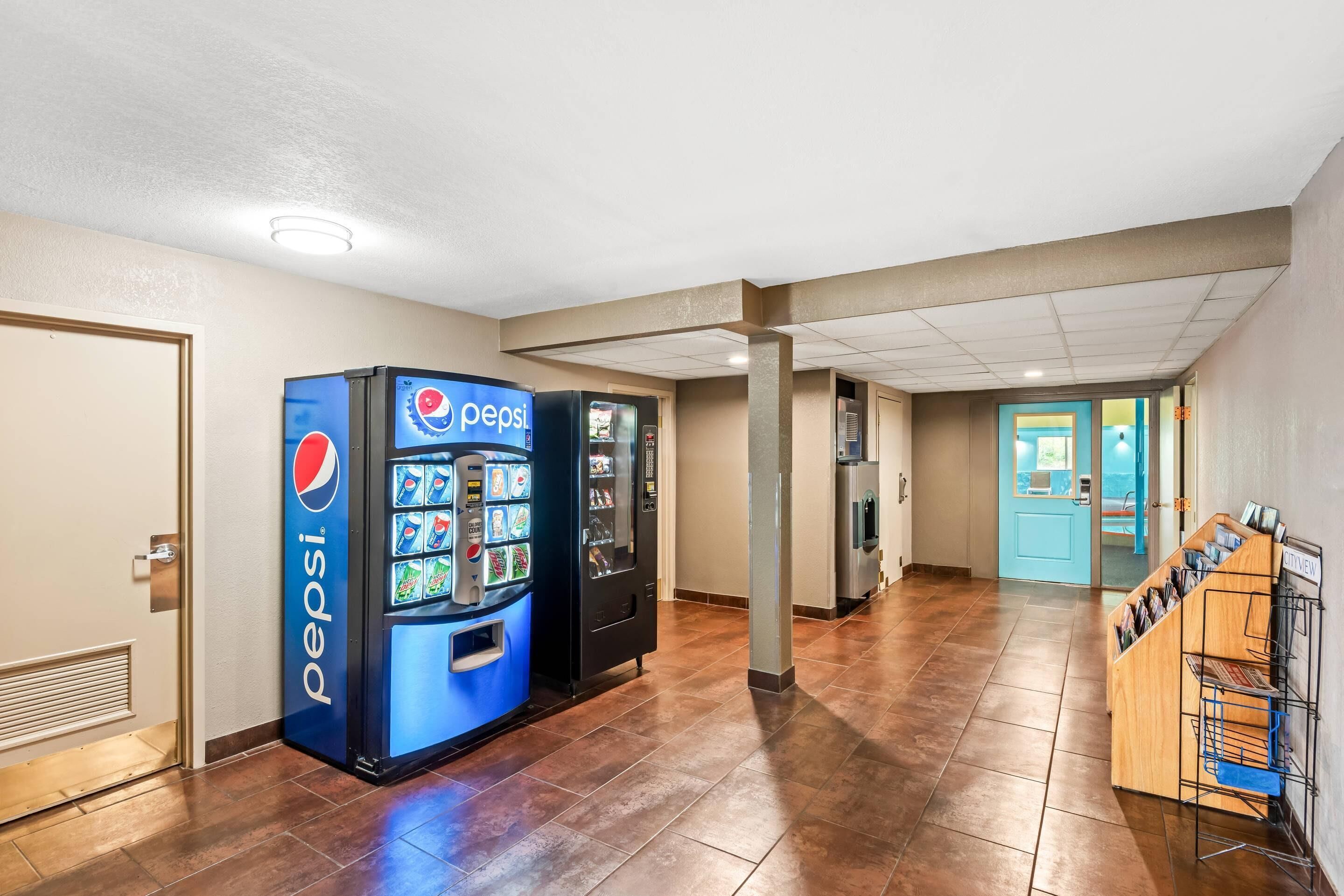 A hallway with a Pepsi vending machine, a bulletin board, and a blue door.