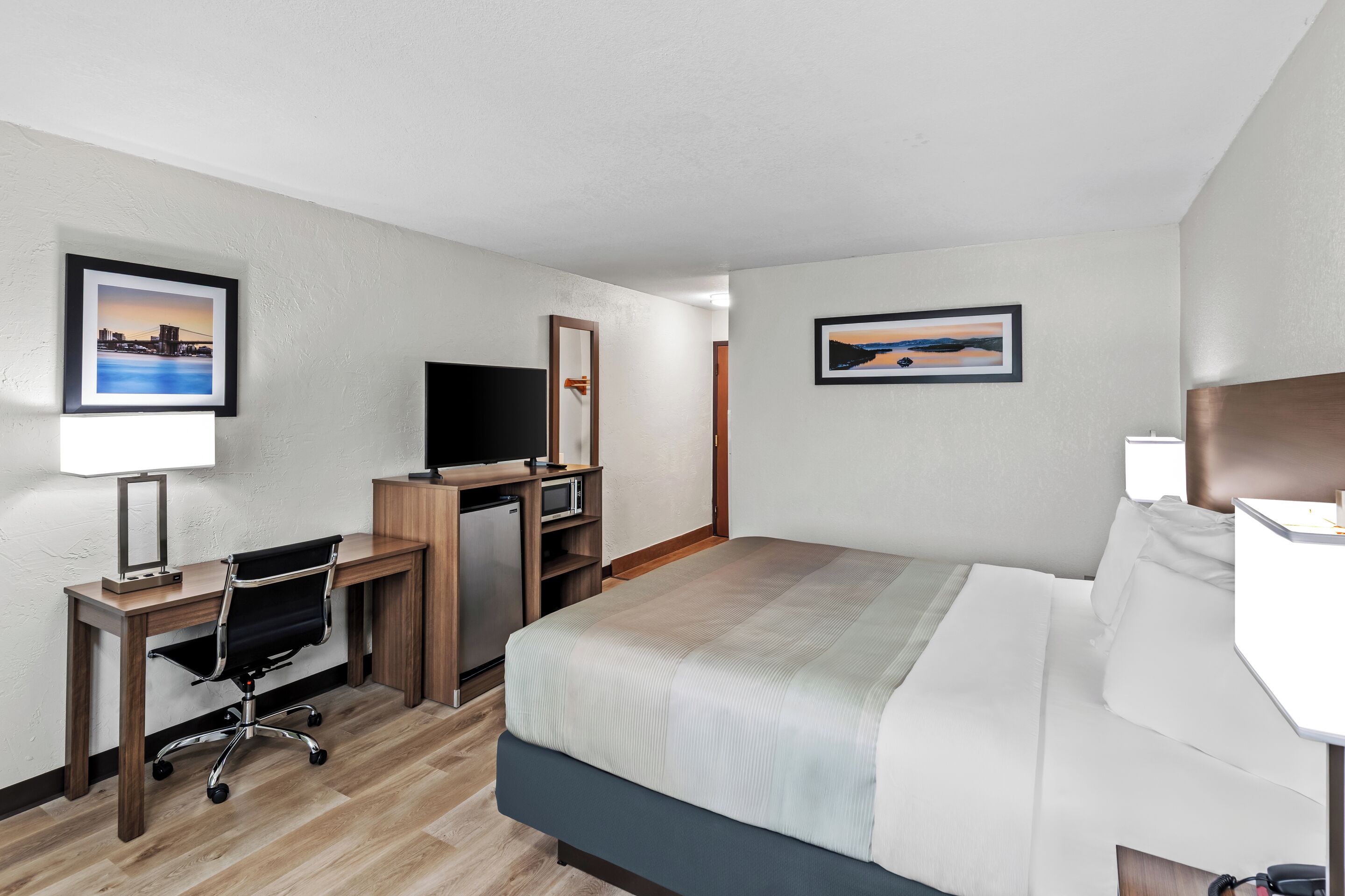 A hotel room with a bed, desk, chair, television, and two framed pictures on the walls.