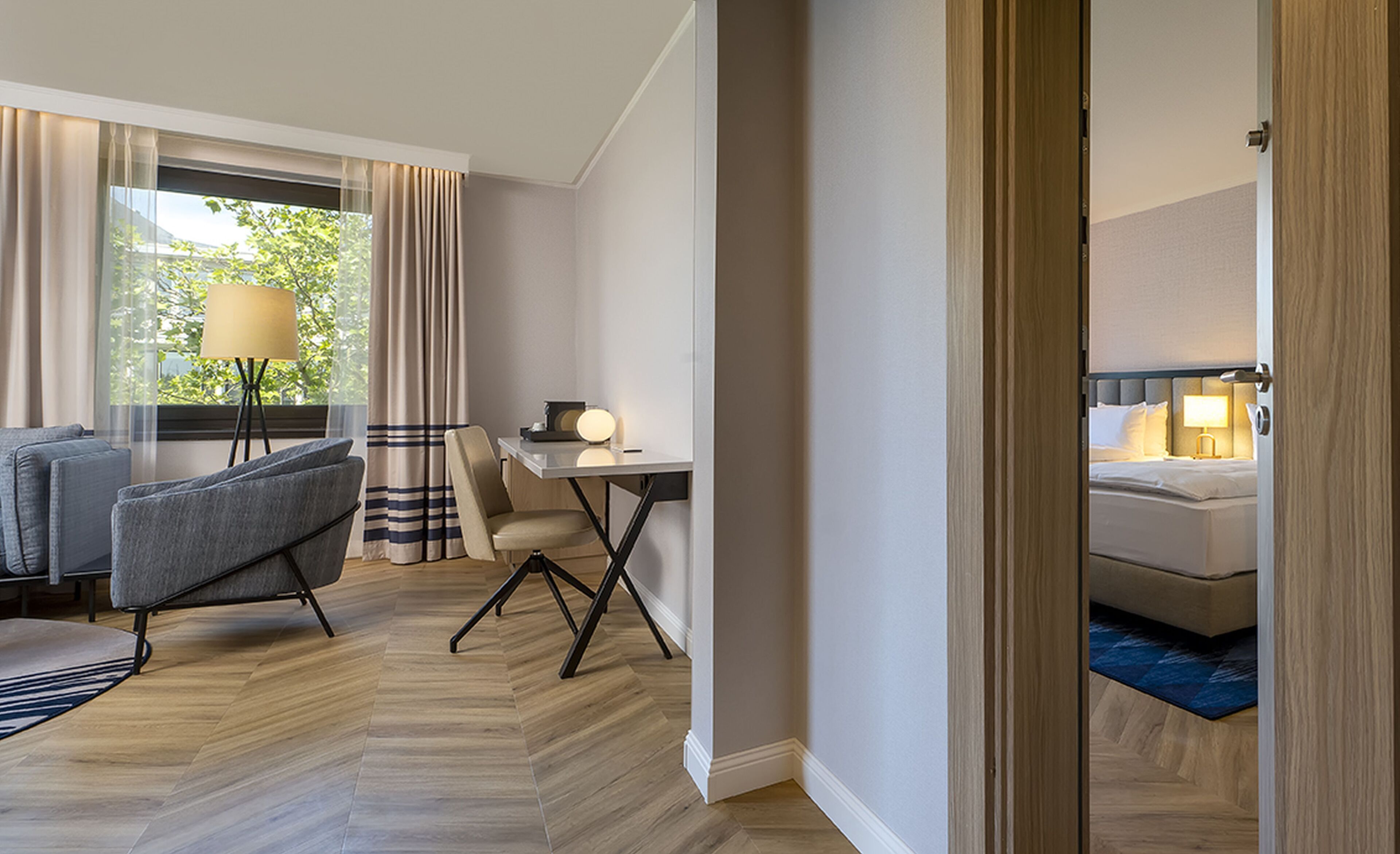 A hotel room with a bed, a desk, a chair, a sofa, and a lamp.