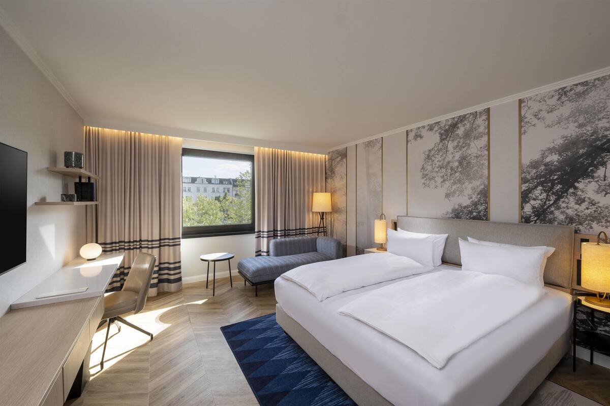 Una habitación de hotel con una cama grande, un escritorio, una silla, una mesita y un televisor.