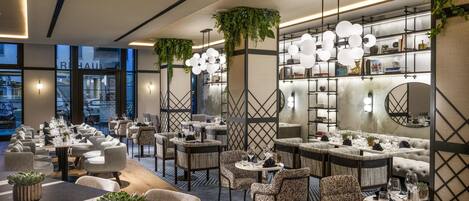 Un restaurant moderne doté de plusieurs espaces de restauration, notamment des tables rondes et des banquettes, ainsi qu’un bar avec un comptoir haut.