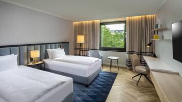 Habitación de hotel con dos camas, un escritorio, una silla, una mesita y una ventana con cortinas.