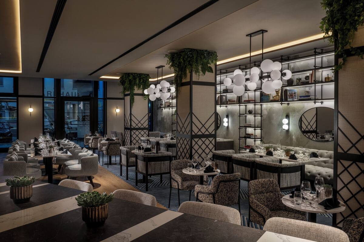 Un restaurante moderno con varias zonas de comedor, incluyendo mesas redondas y cabinas, además de una zona de bar con mostrador.