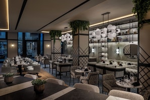 A modern restaurant with multiple dining areas, including round tables and booths, and a bar area with a counter. - DoubleTree by Hilton Berlin Ku'damm (Berlin)
