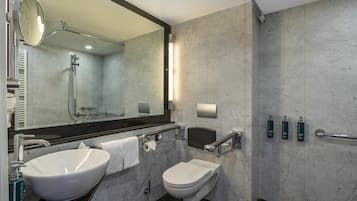 A modern bathroom with a large mirror, two sinks, a toilet, and a shower.