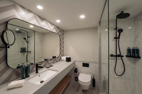 A modern bathroom with a large mirror, a sink, a toilet, and a shower area. - DoubleTree by Hilton Berlin Ku'damm (Berlin)
