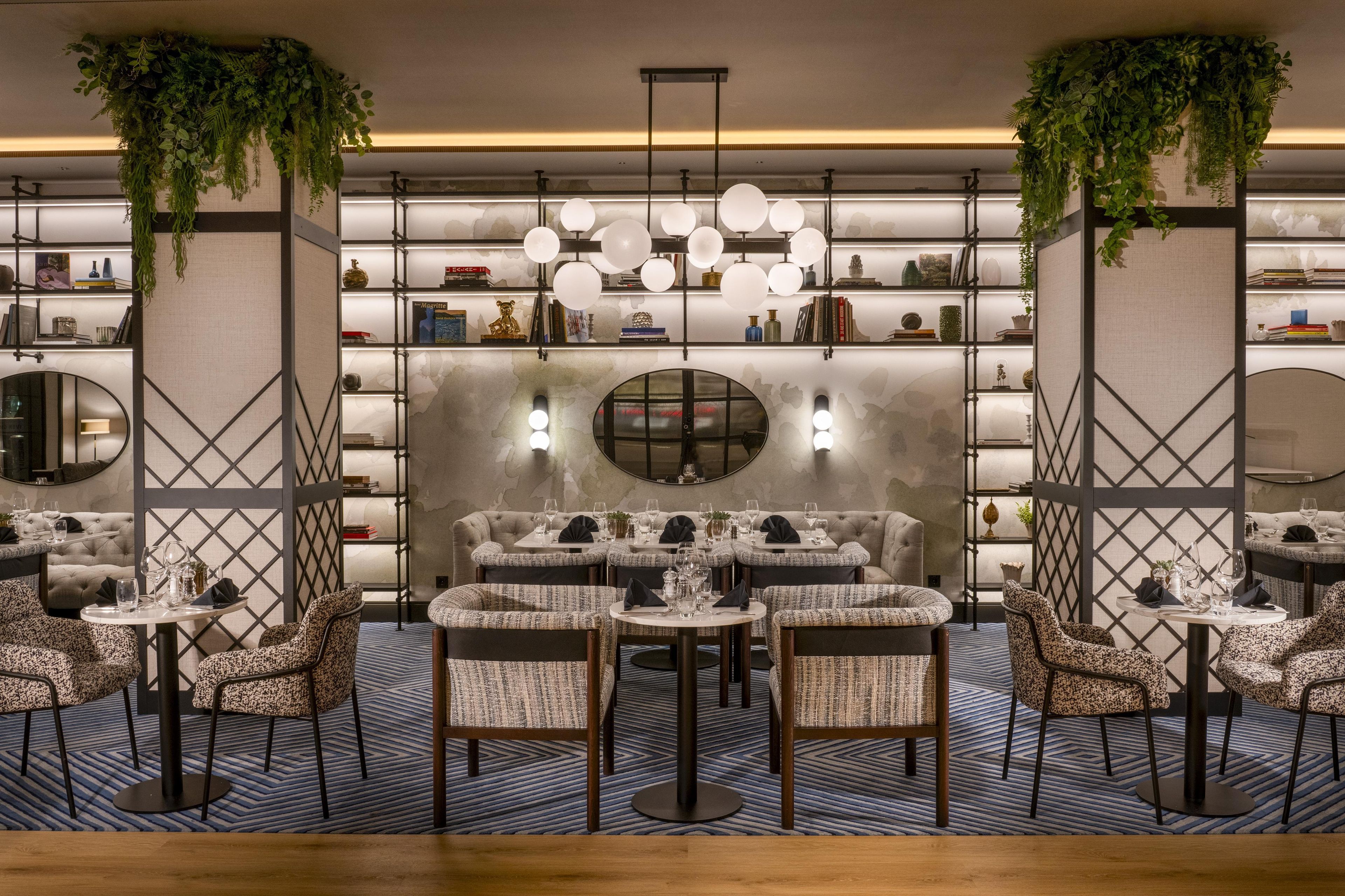 Um interior moderno com uma área de estar central, rodeada por estantes de livros e iluminação decorativa.