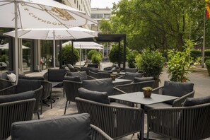 An outdoor seating area with wicker chairs and tables, umbrellas, and potted plants. - DoubleTree by Hilton Berlin Ku'damm (Berlin)