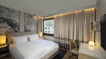 A hotel room with a large bed, a desk, a chair, a TV, and a window with curtains.