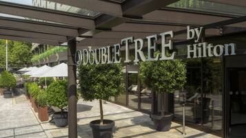 A hotel entrance with a sign reading 'DOUBLETREE by Hilton' and potted trees in front.