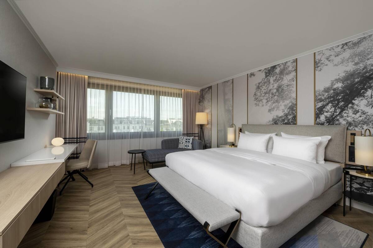 Habitación de hotel con una cama grande, un escritorio con computadora, una silla, una mesita y un televisor.