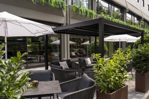 An outdoor seating area with wicker furniture, white umbrellas, and potted plants. - DoubleTree by Hilton Berlin Ku'damm (Berlin)