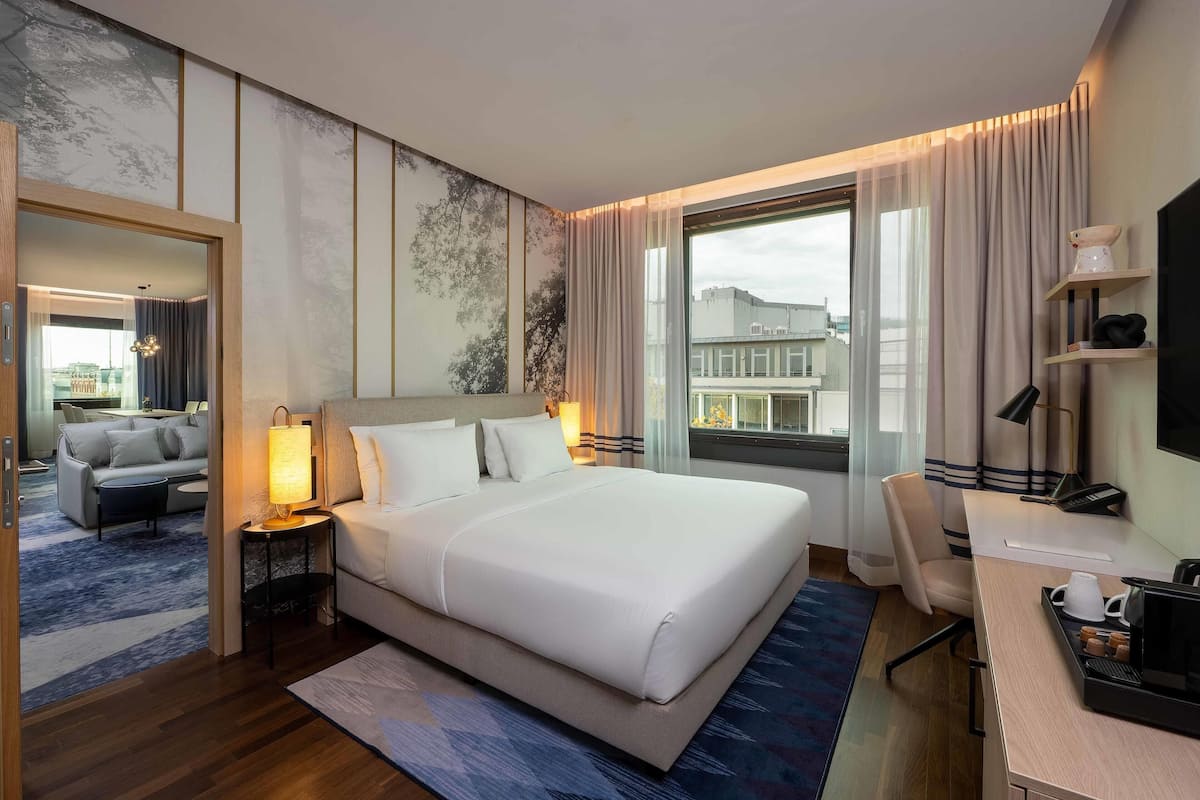 Habitación de hotel con una cama grande, un escritorio con silla, televisión y ventana con cortinas.