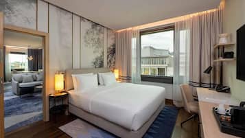 Ein Hotelzimmer mit einem großen Bett, einem Schreibtisch mit Stuhl, einem Fernseher und einem Fenster mit Vorhängen.