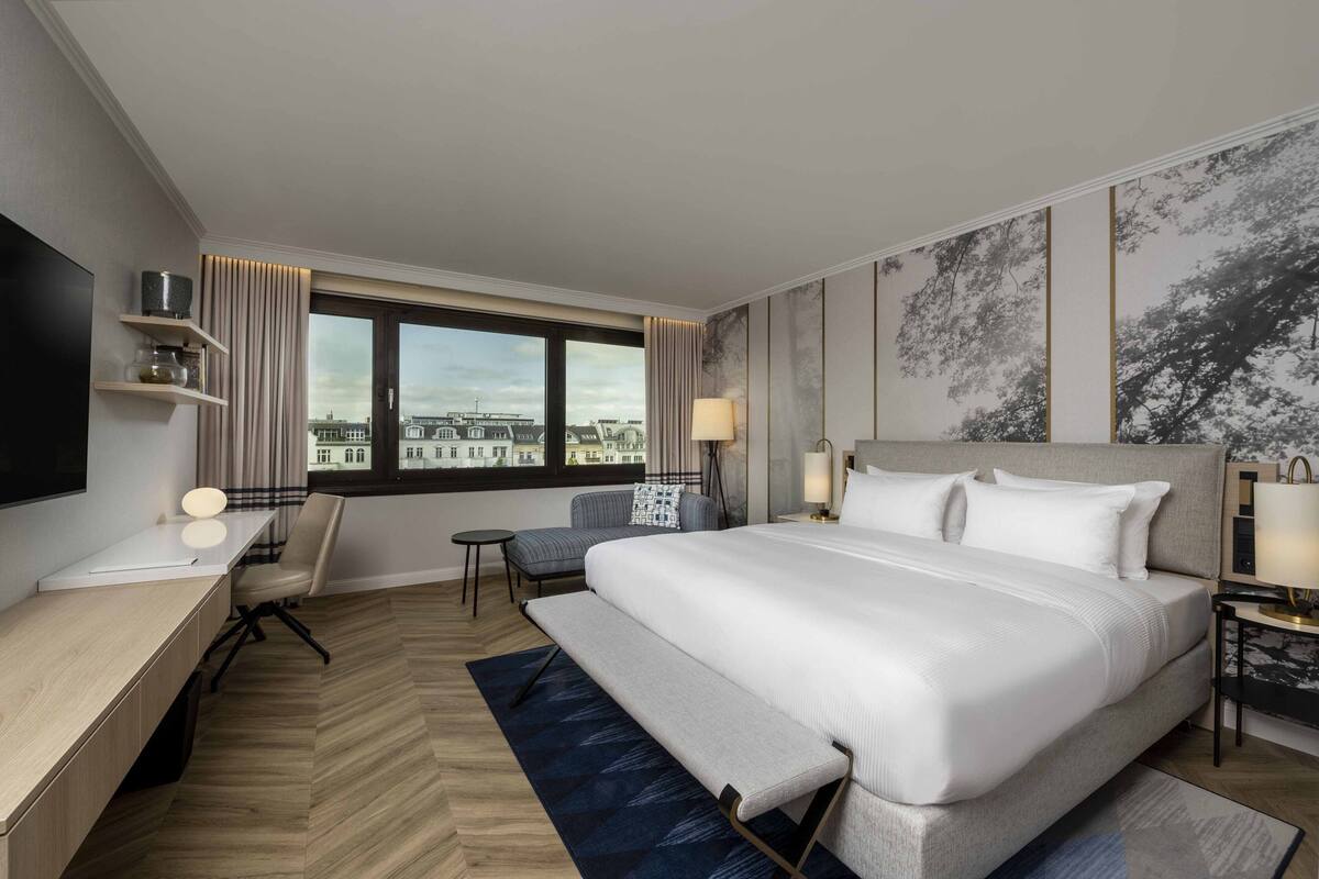 Habitación de hotel con una cama grande, un escritorio, una silla, una mesita y vistas a la ciudad.