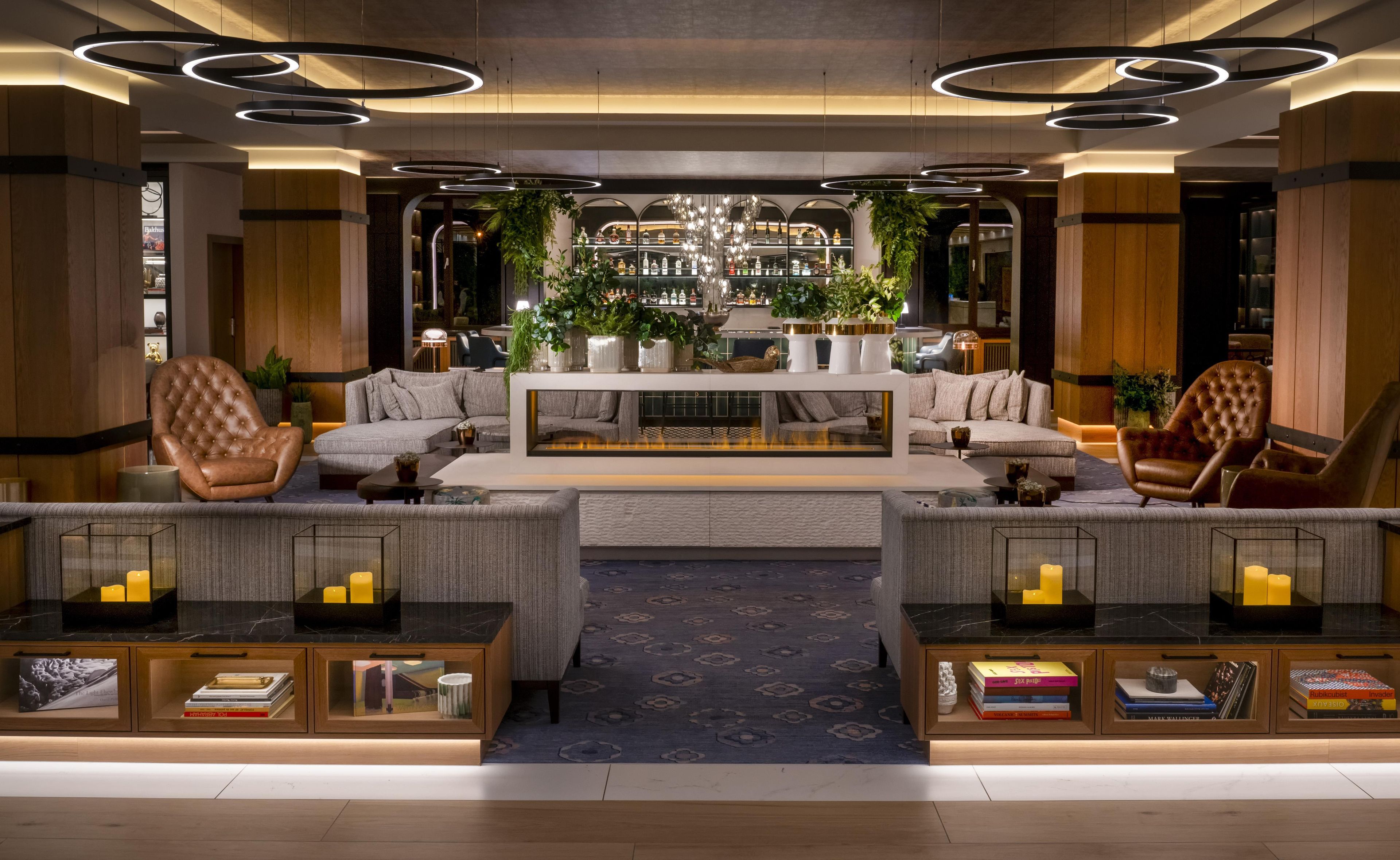 Ein moderner Loungebereich mit Ledersesseln, einer zentralen Couch, einer Bar mit Flaschen und einer Chandelier.