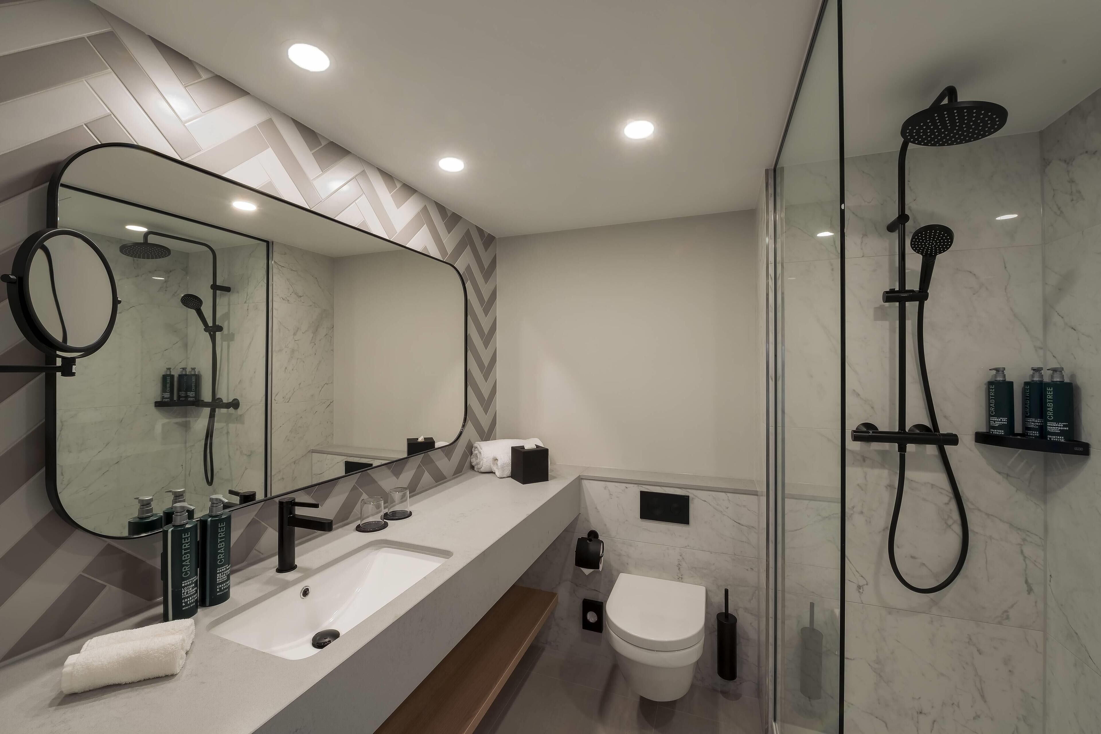 A modern bathroom with a large mirror, a sink, a toilet, and a shower area.