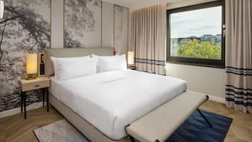 A neatly arranged hotel room with a large bed, bedside lamps, a bench, and a view of buildings through the window.