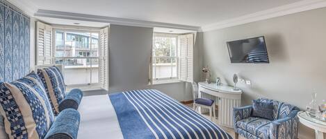 Habitación de hotel con una cama grande, un escritorio, una silla y un televisor en la pared.