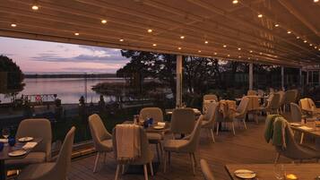 An outdoor dining area with tables and chairs, overlooking a body of water.