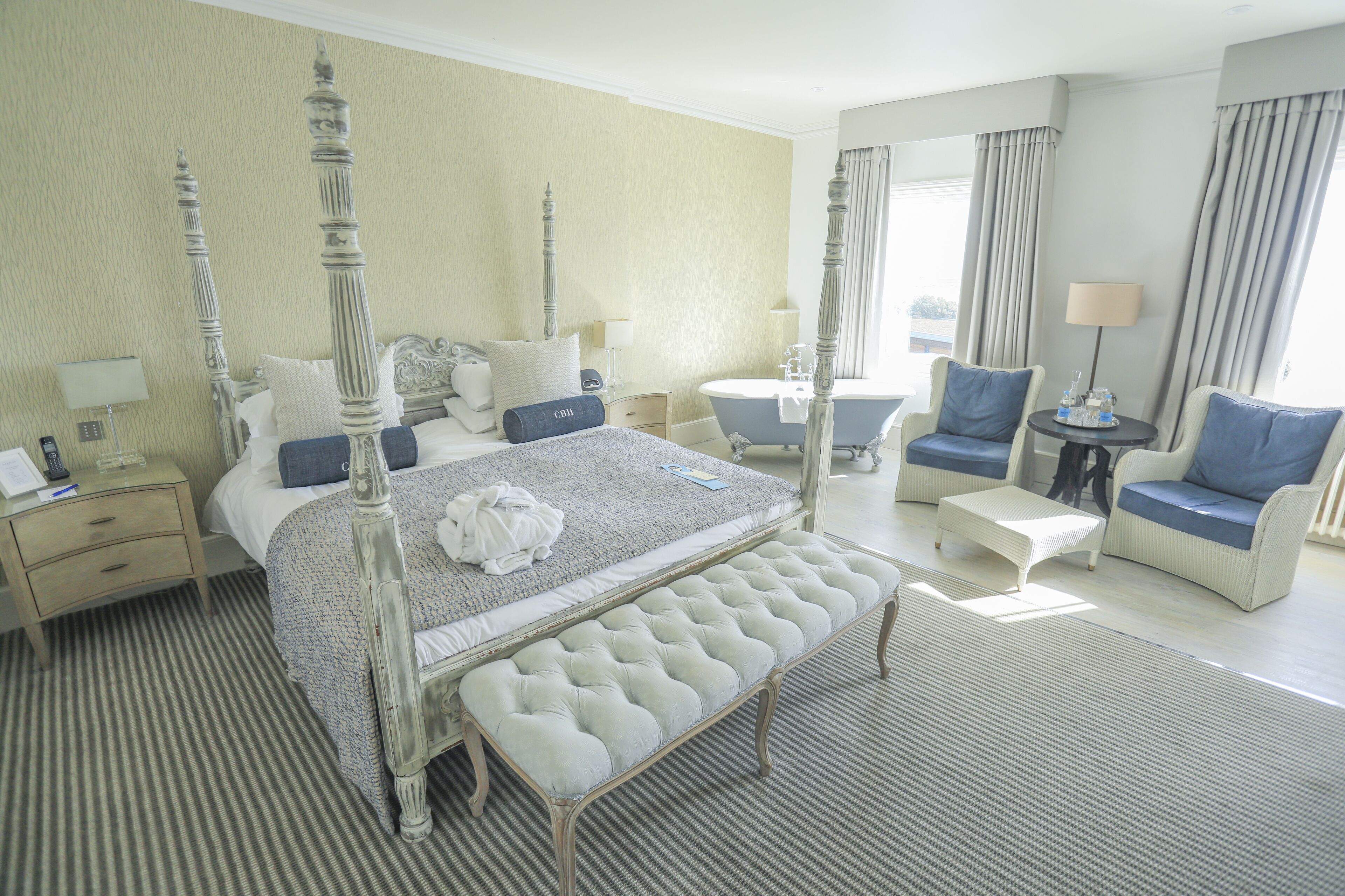 Une chambre d’hôtel spacieuse, dotée d’un lit à baldaquin, d’un coin salon avec un canapé et des fauteuils, d’une petite table ronde et d’une salle de bain séparée avec une baignoire.
