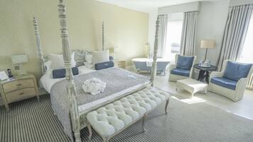 Une chambre d’hôtel spacieuse, dotée d’un lit à baldaquin, d’un coin salon avec un canapé et des fauteuils, d’une petite table ronde et d’une salle de bain séparée avec une baignoire.
