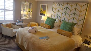 A hotel room with a large bed, a sitting area with a chair and a small table, a mirror, and a wall with a geometric pattern.