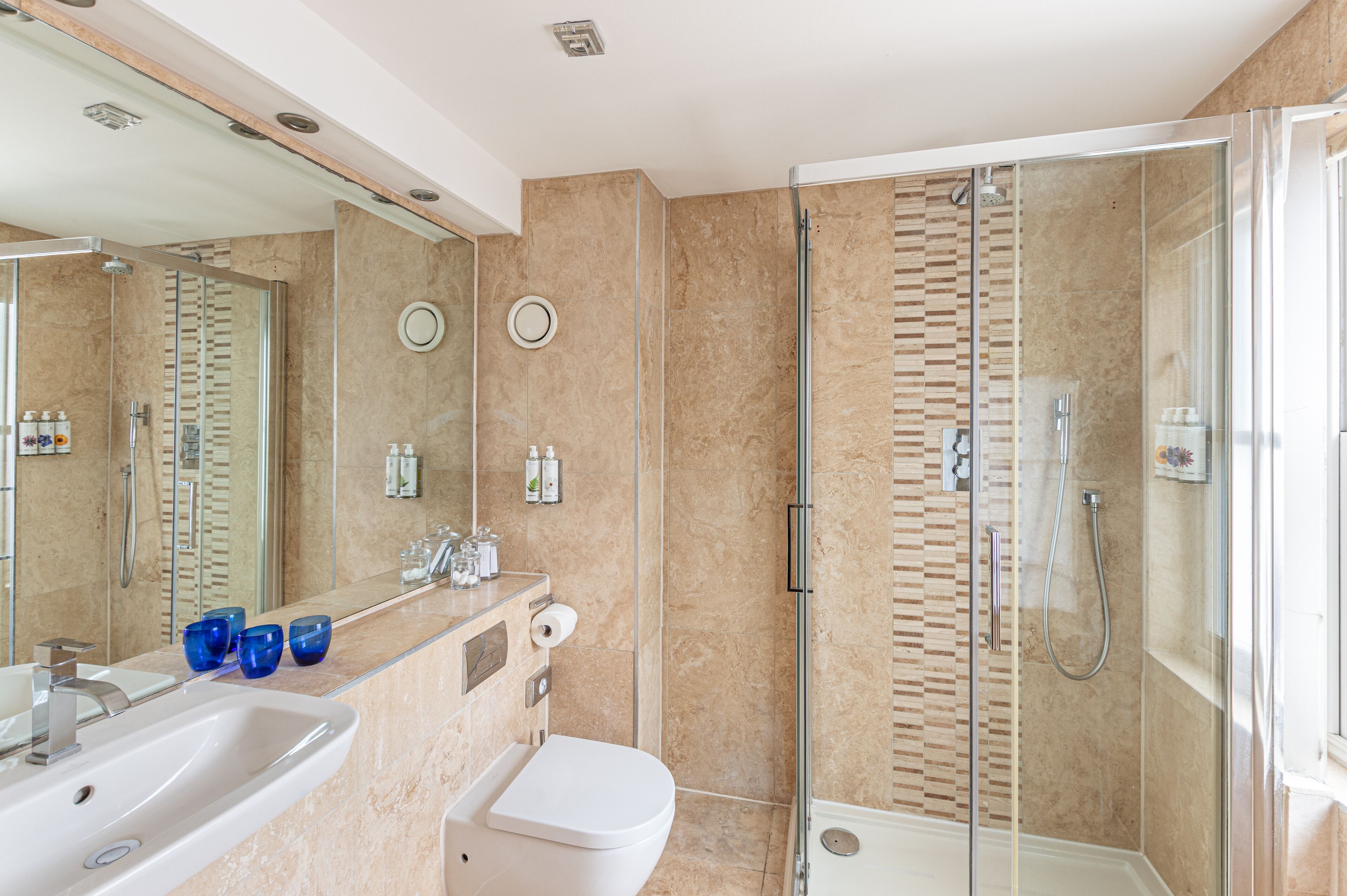 A modern bathroom with a glass-enclosed shower, a sink with a mirror, and toiletries on the counter.