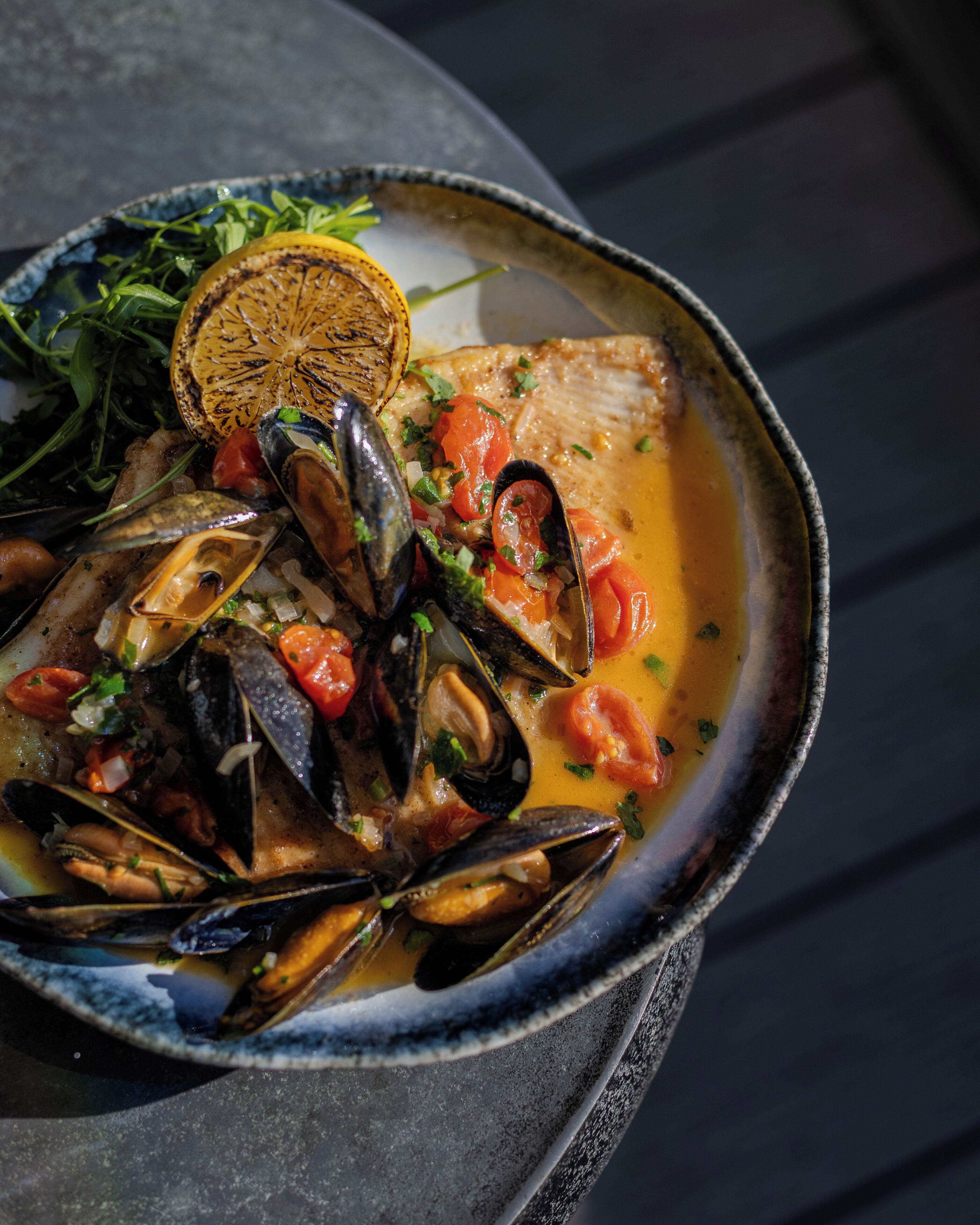 A seafood dish with mussels, tomatoes, and herbs in a bowl.