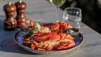 A lobster dish on a plate with a glass of white wine and two salt shakers on a table.